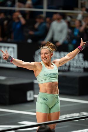 Athlete in mint green outfit celebrating with arms spread wide during CrossFit competition.