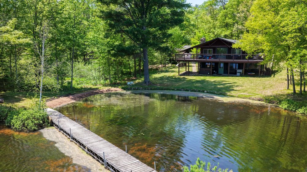 Charming log cabin retreat with private pond, stone pathway, and mature trees in a serene setting.