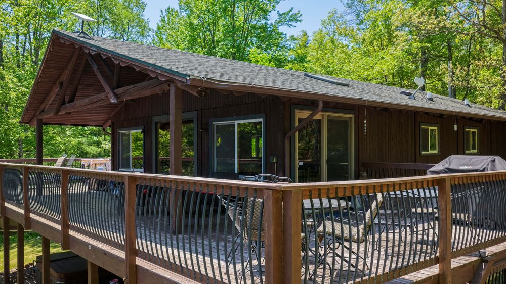Spacious wooden deck with outdoor seating area attached to a cozy brown log cabin in the woods.