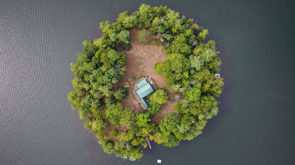 Aerial view of a small forested island with a cabin surrounded by calm water.