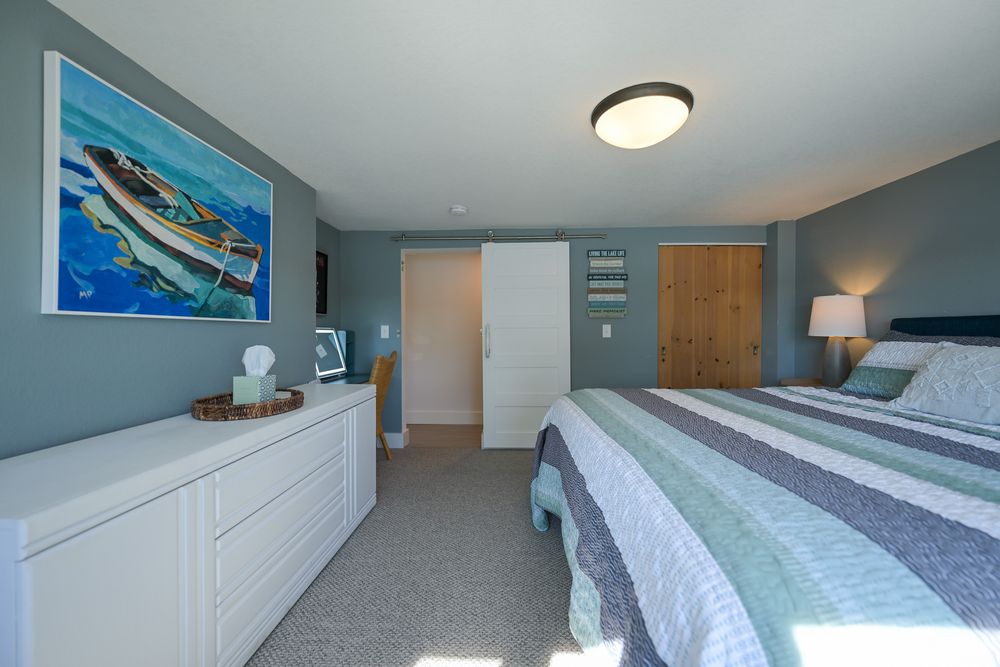Bright bedroom with a striped bed, white dresser, coastal boat painting, gray walls, and a wooden door.