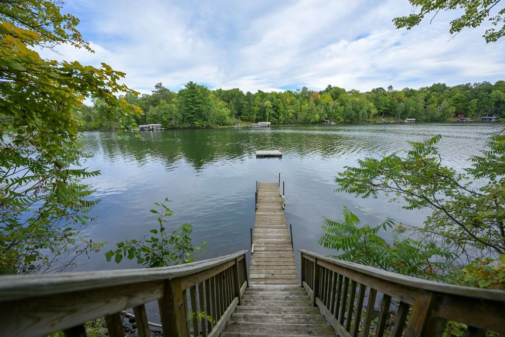 Wooden dock staircase leading to a serene lake surrounded by lush green trees under a partly cloudy sky.
