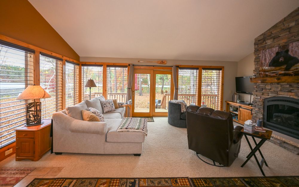 Cozy living room with vaulted ceiling, stone fireplace, plush sectional sofa, leather recliner, and large windows with garden door access.