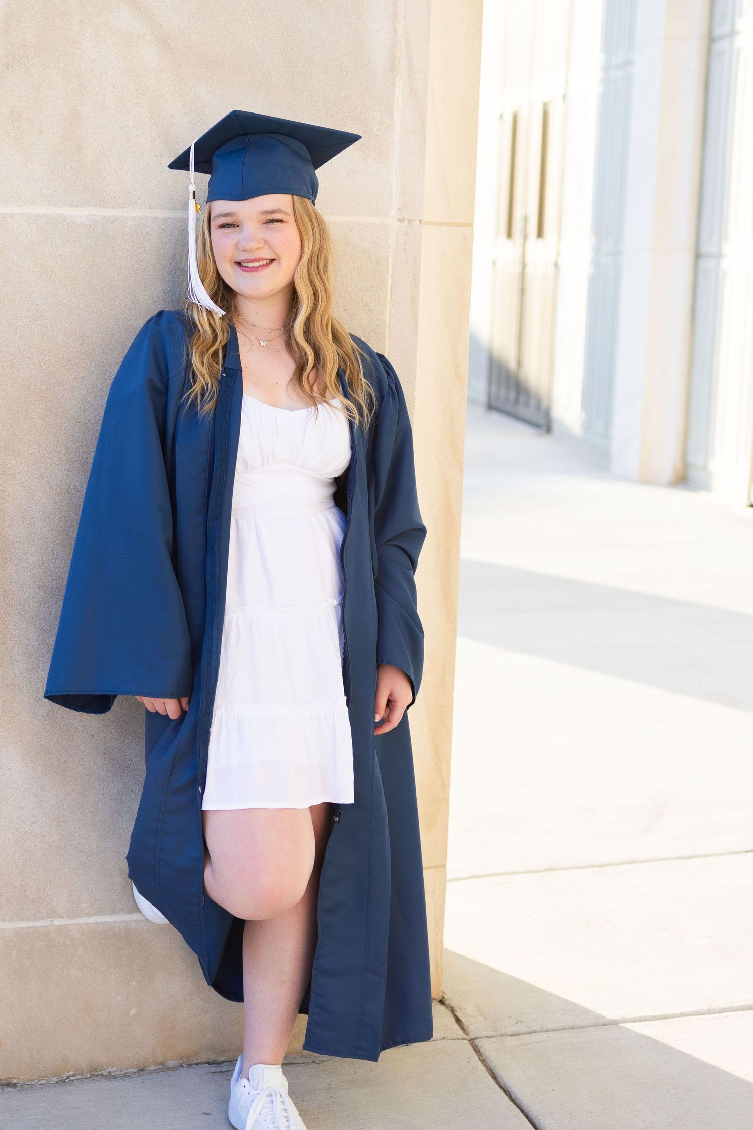 High school senior in cap/gown leaning against column.