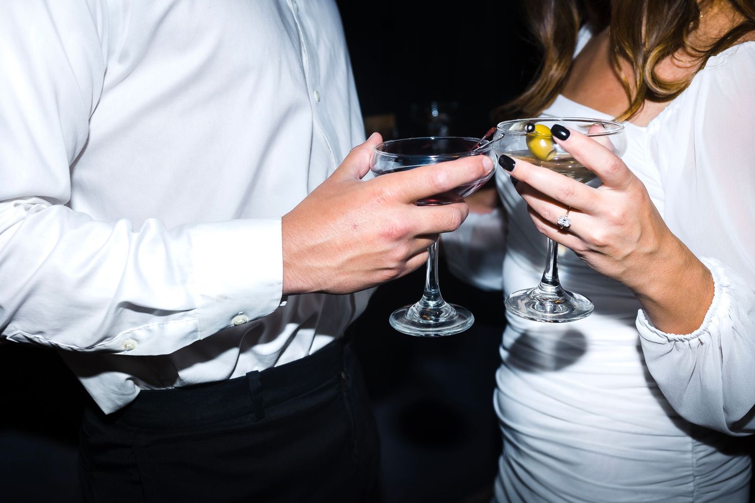 man in white and black dress clothes and woman in white cheers champagne flutes