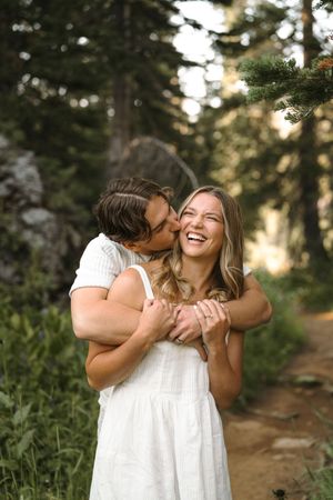 A joyful couple sharing intimate moments and laughter while embracing on a forest path at sunset.