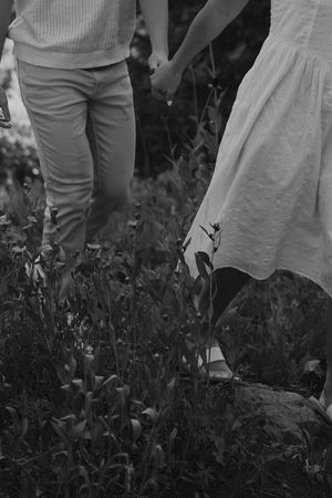 A grayscale close-up of legs walking through tall wildflowers in a meadow.