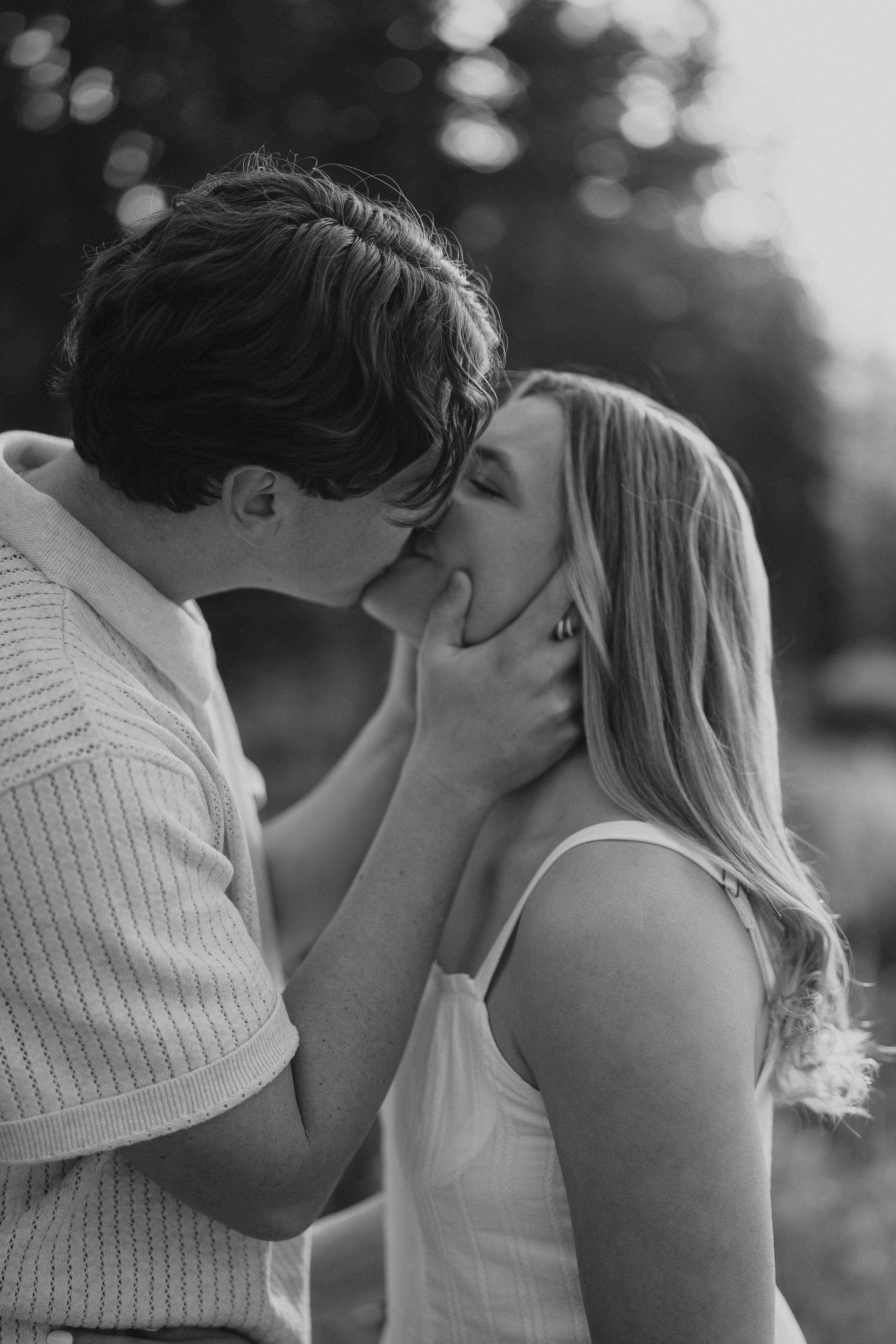 A tender black and white romantic moment shared between a couple in casual clothing outdoors with soft bokeh lighting.