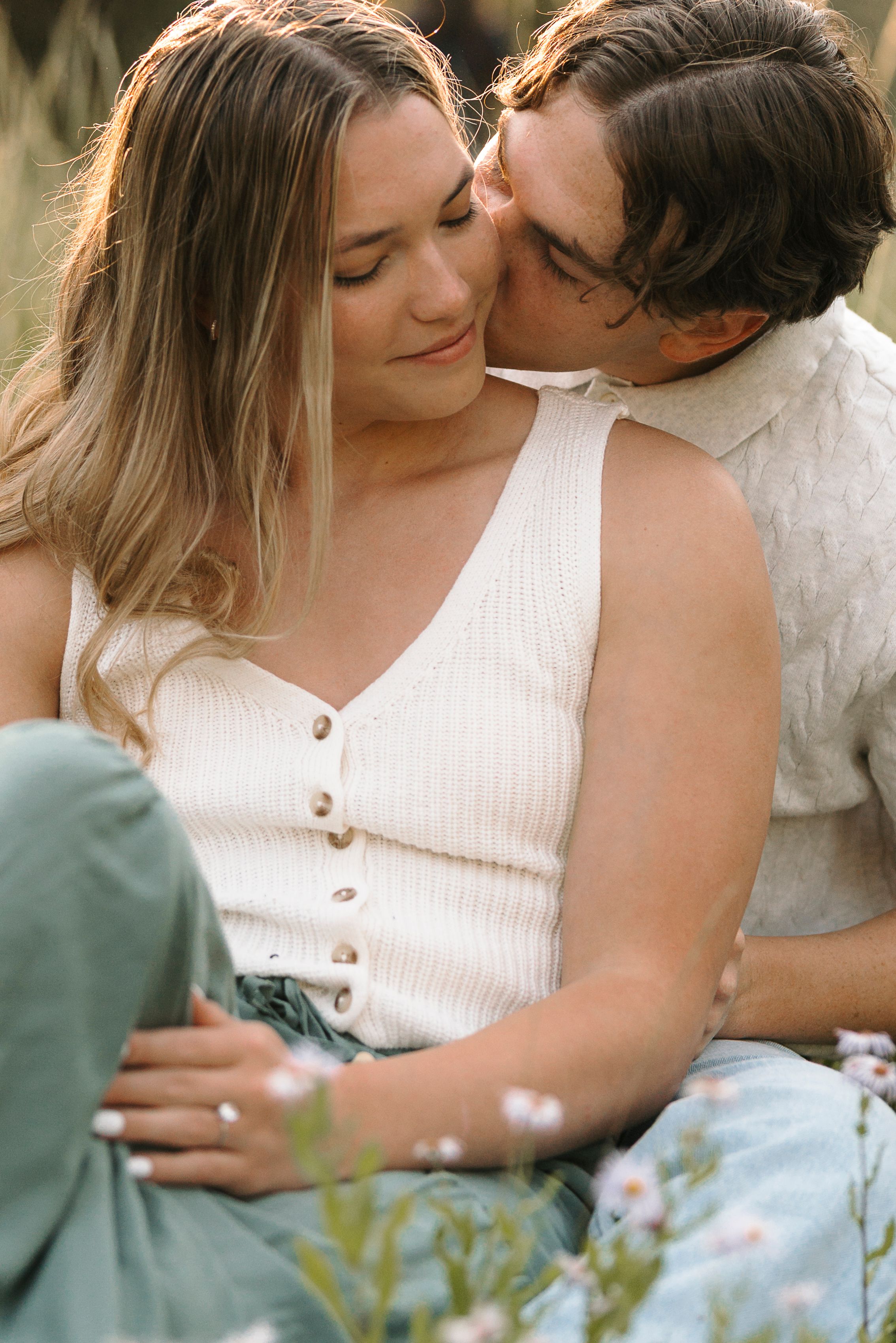 A tender romantic moment shared between a couple outdoors, with her wearing a white button-up tank top.