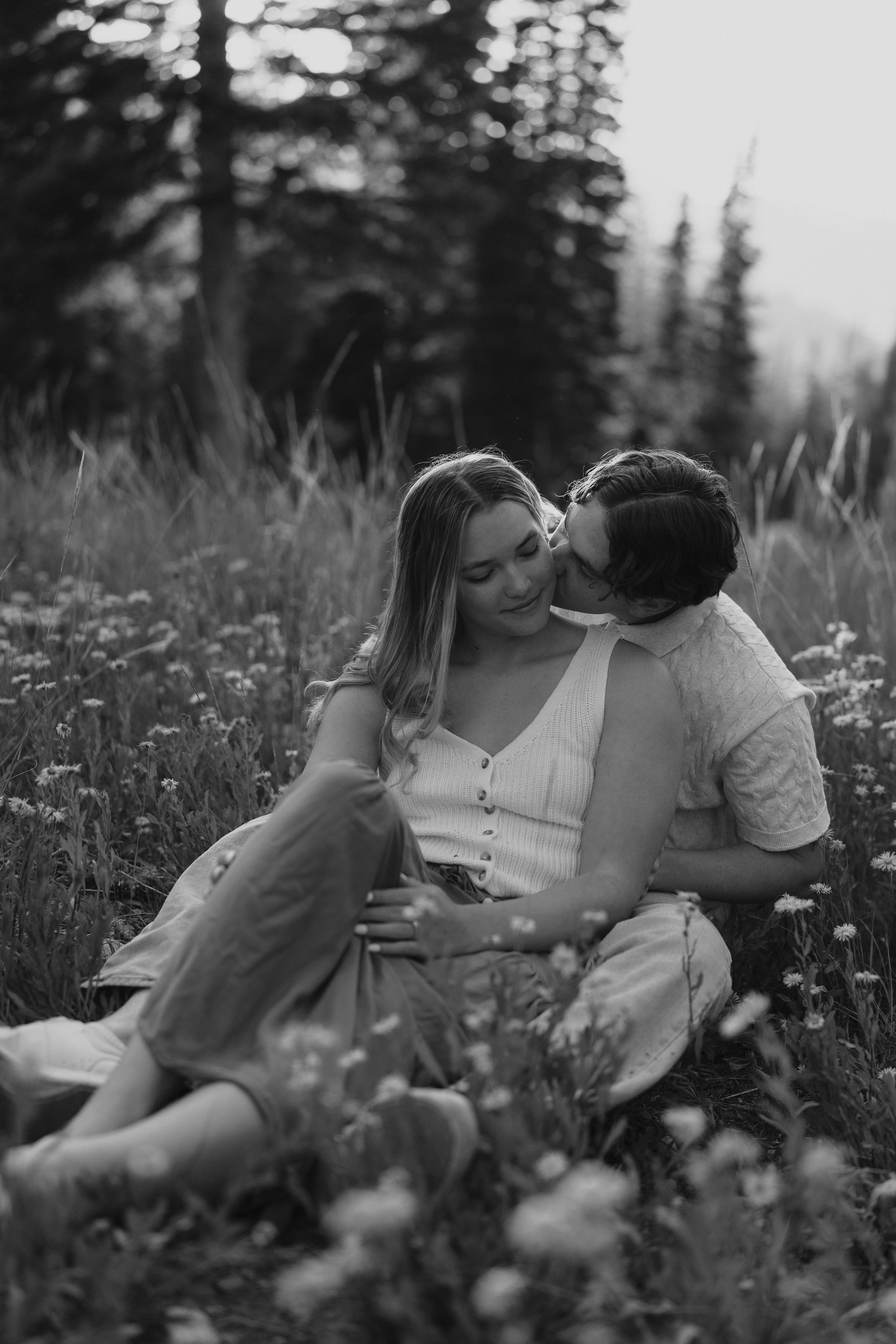 Black and white photos of couple lying in wildflower meadow surrounded by tall grass in peaceful mountain setting.