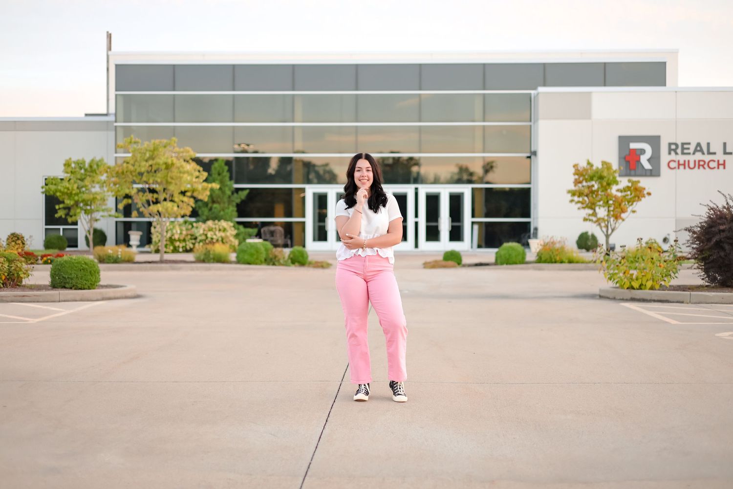Casual outdoor portrait in pink pants standing in front of a modern office building.