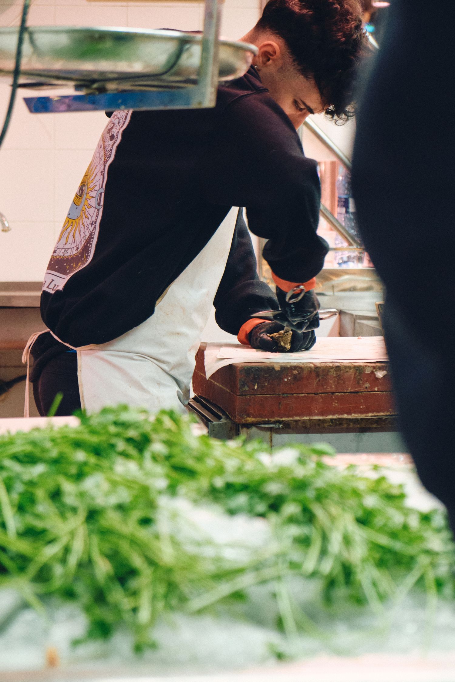 Worker preparing fresh produce at market station with greens visible.