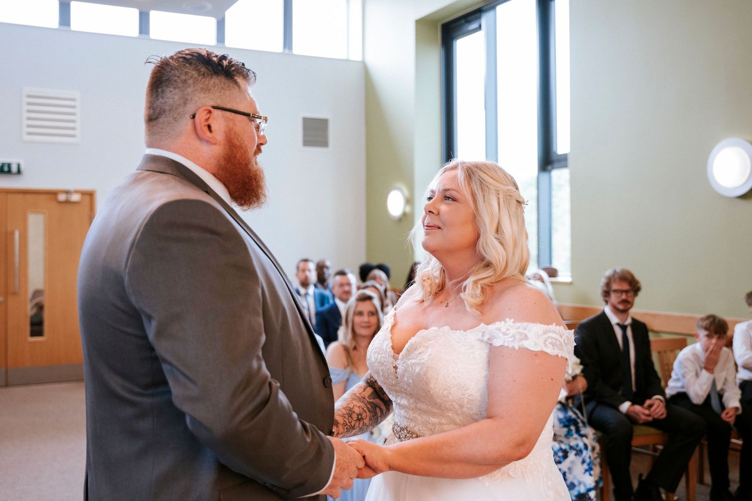 A wedding ceremony takes place in a bright indoor venue as the couple exchanges vows.