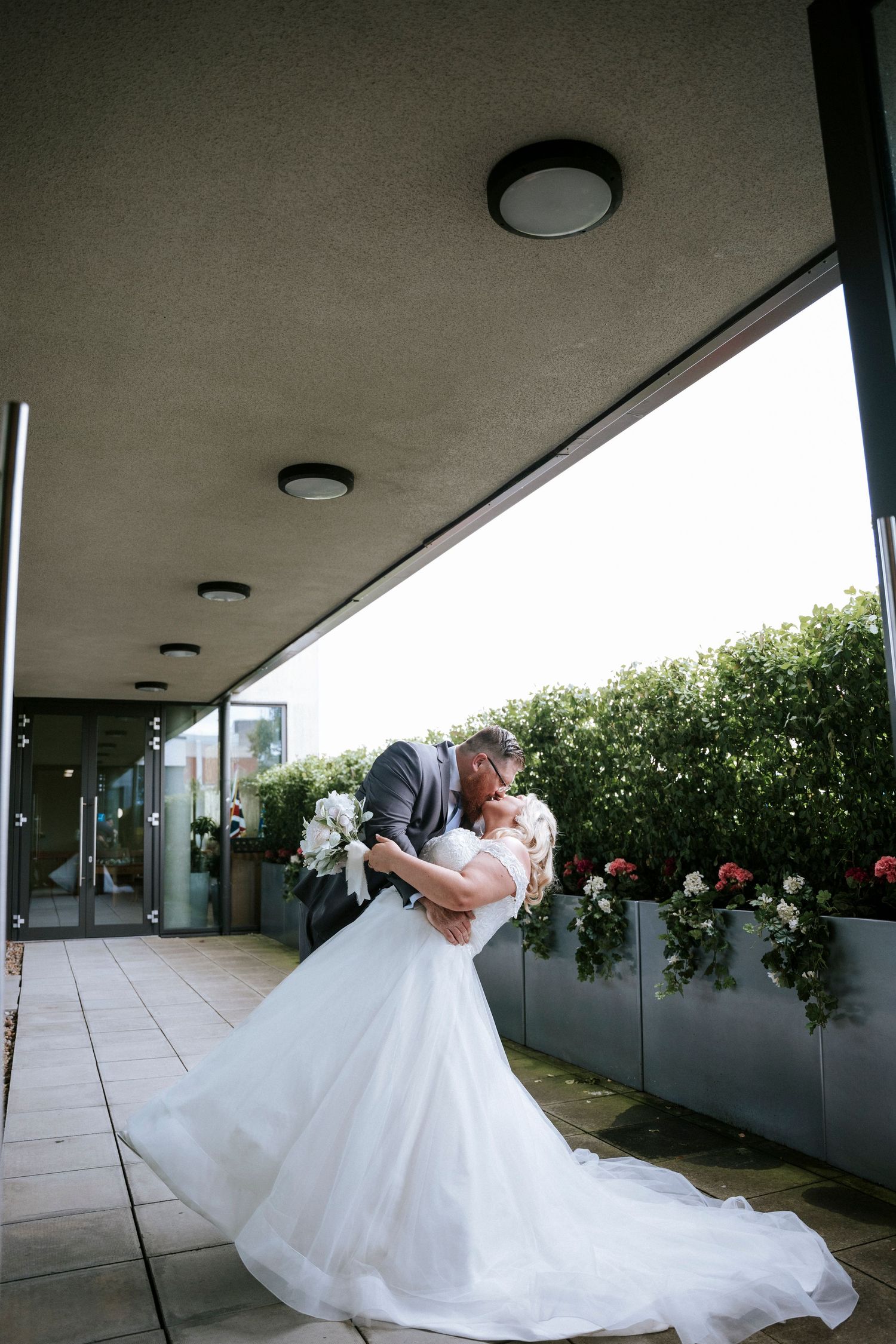 A romantic wedding dip pose on an outdoor patio with greenery in the background.