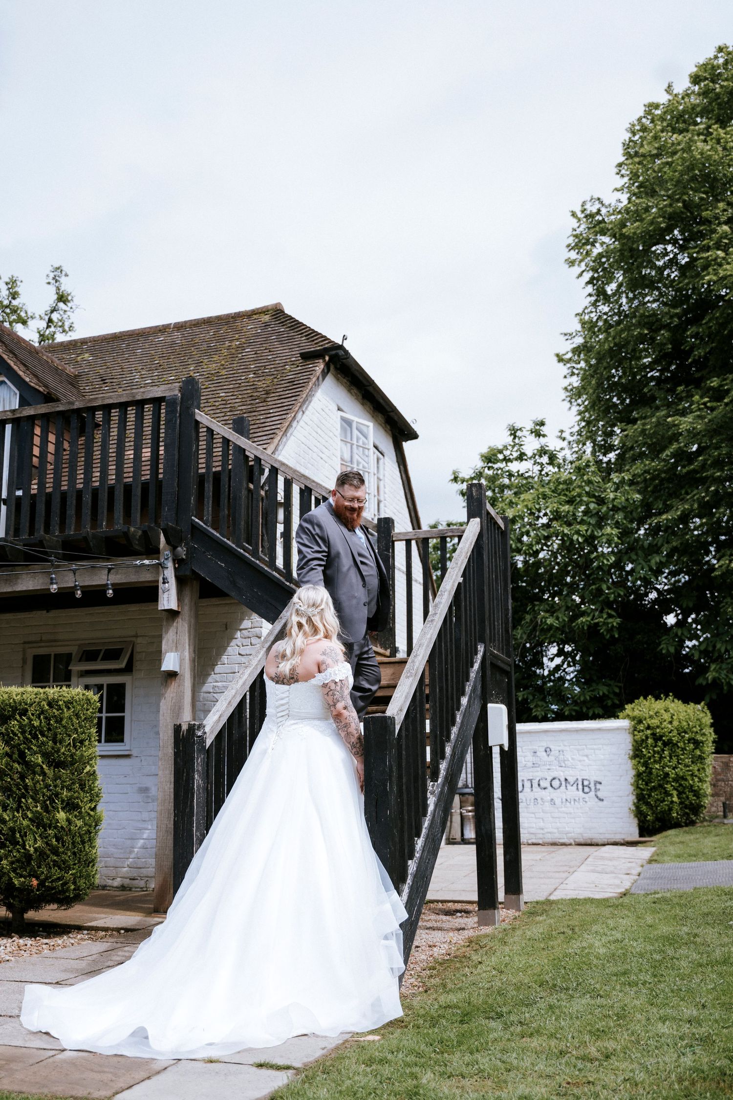 A couple poses on black stairs leading to a white building with a balcony.