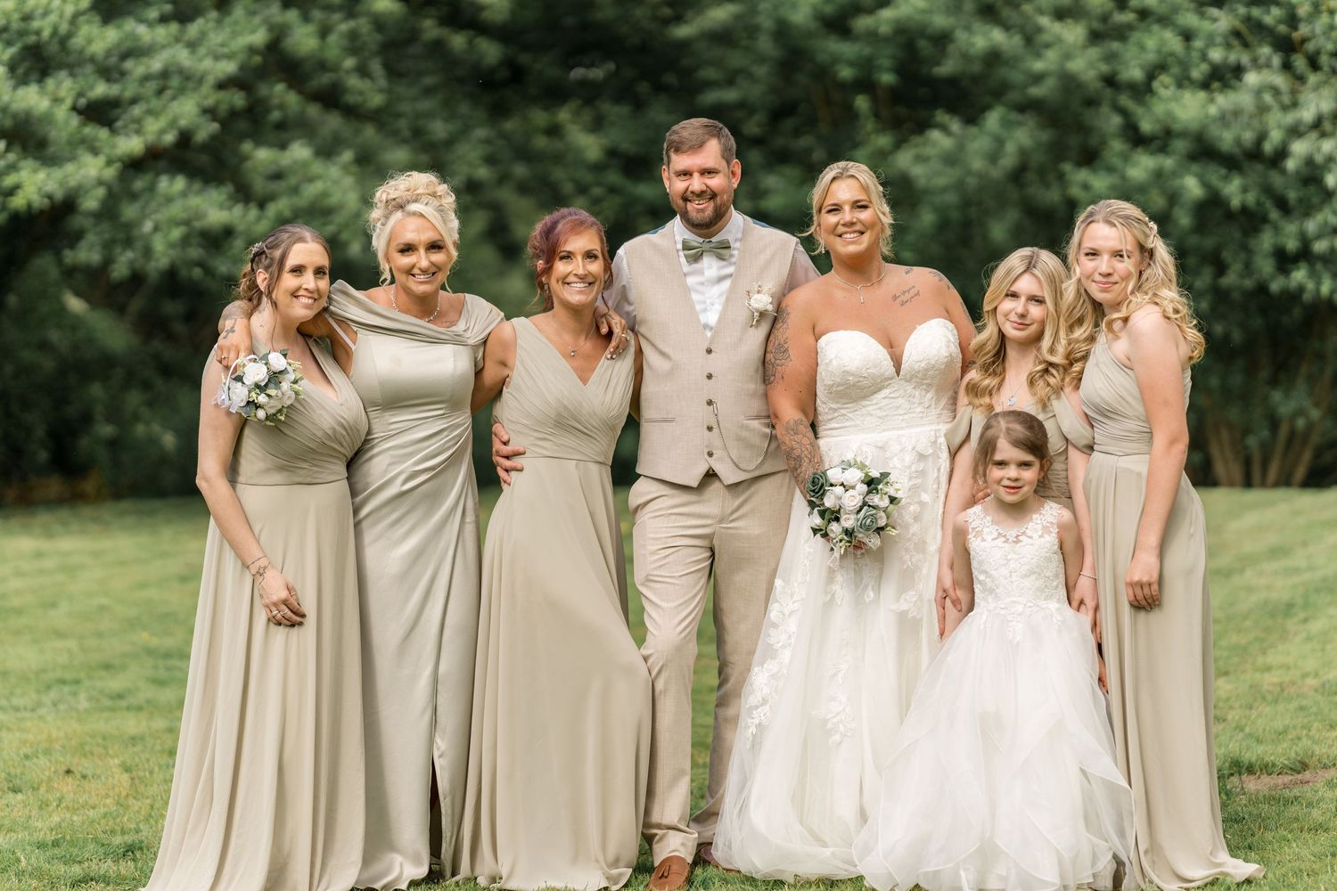 A wedding party poses together outdoors wearing coordinated beige and white formal attire.