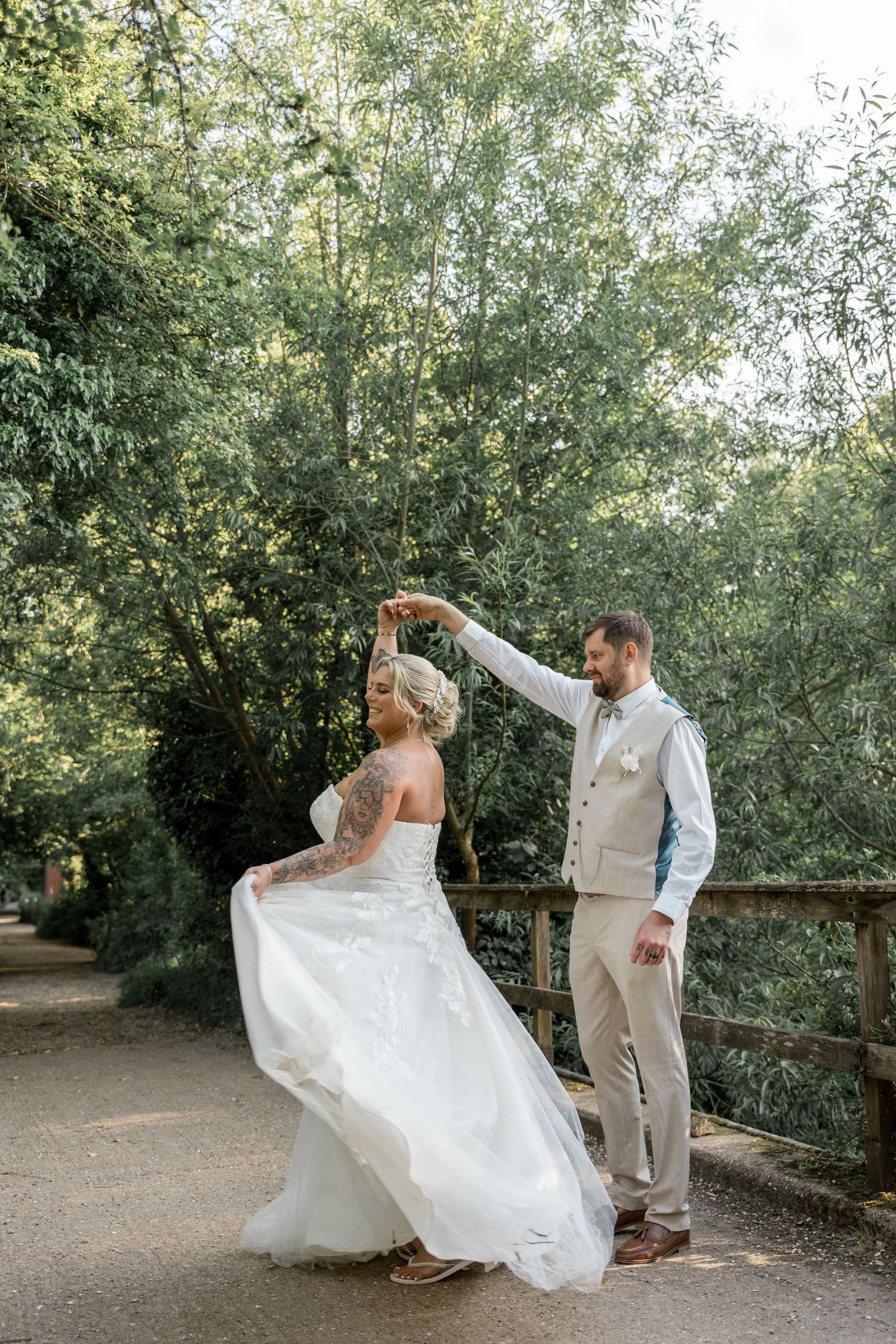 A couple dances on a pathway surrounded by green trees during their wedding photoshoot.