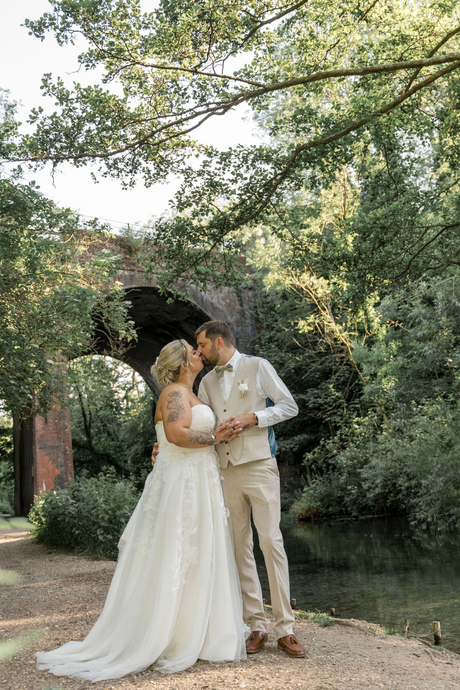 A romantic wedding portrait by a stone bridge with lush greenery in the background.