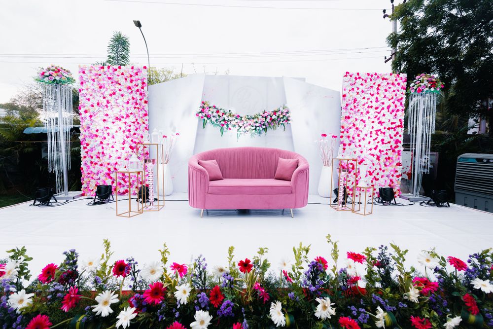 Pink floral wedding stage decoration with pink couch and flower arrangements.