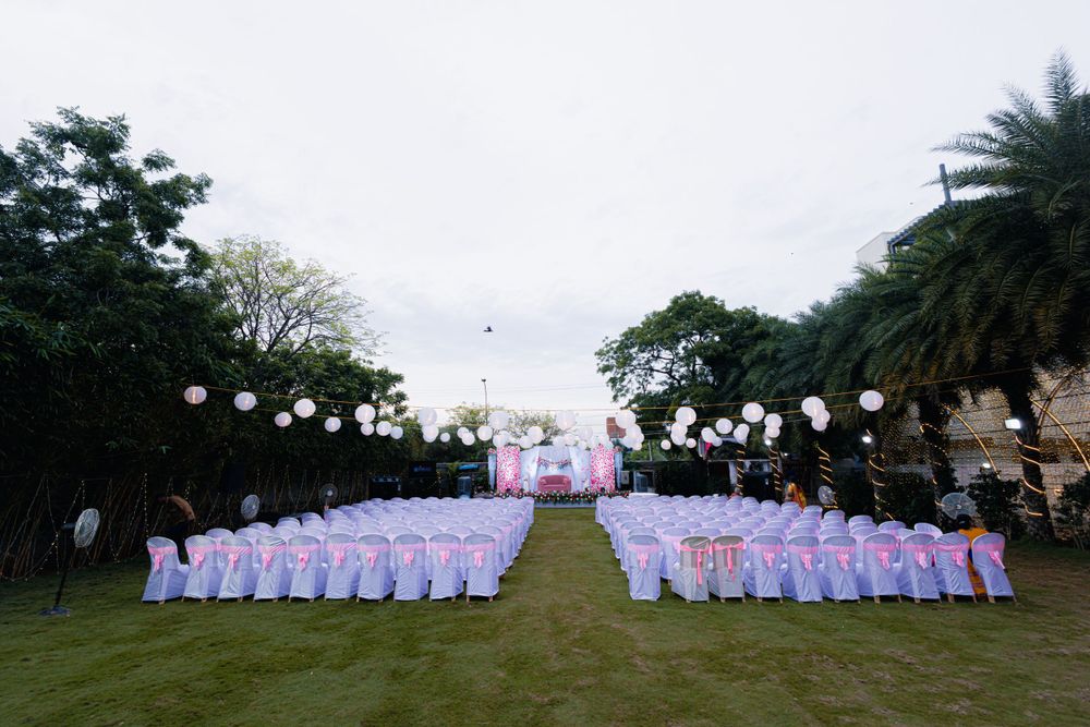 Outdoor wedding ceremony setup with white chairs and pink decor under a cloudy sky.
