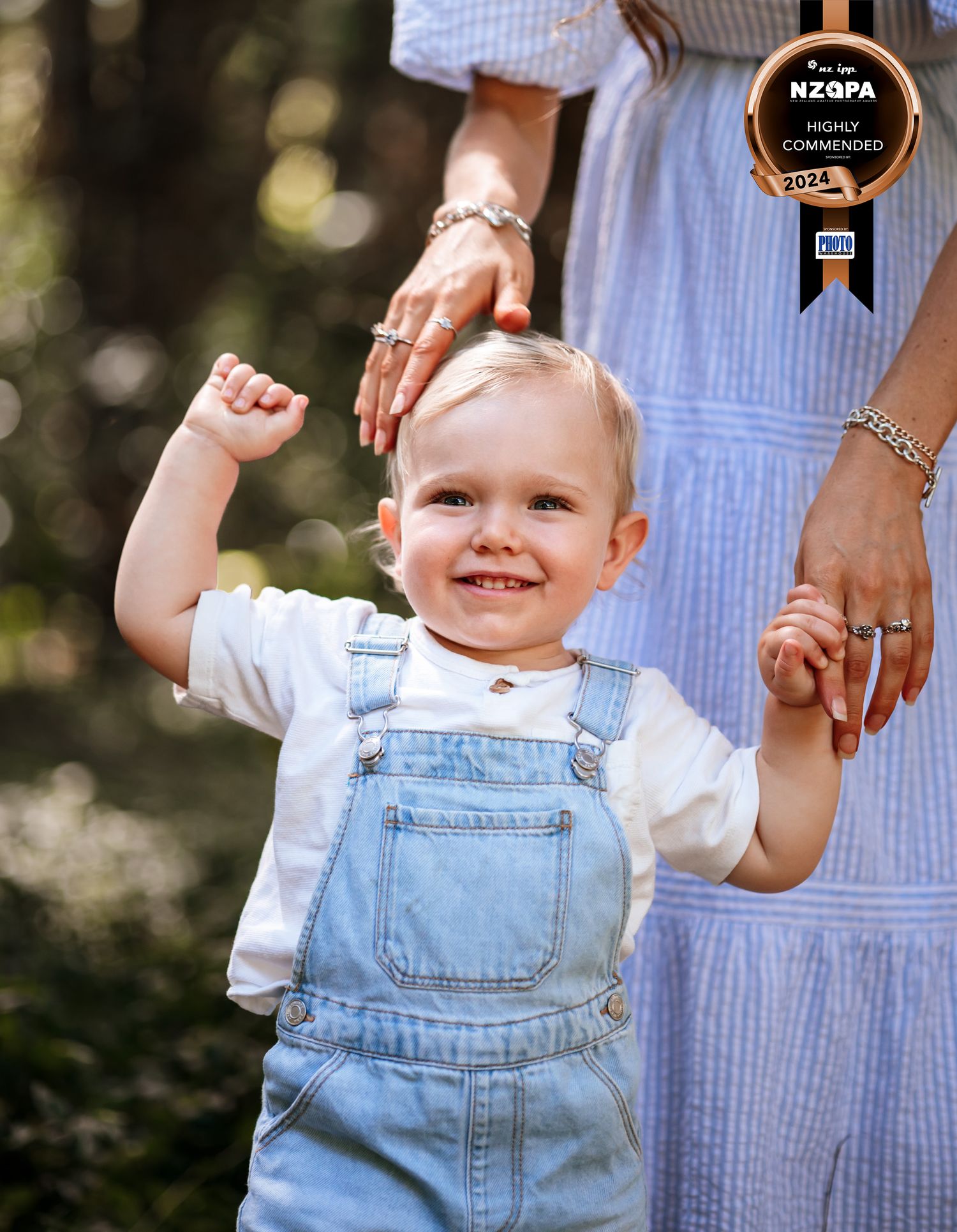 A close up emotive image of a young boy with beaming smile holding his mothers hand while the mother strokes his hair