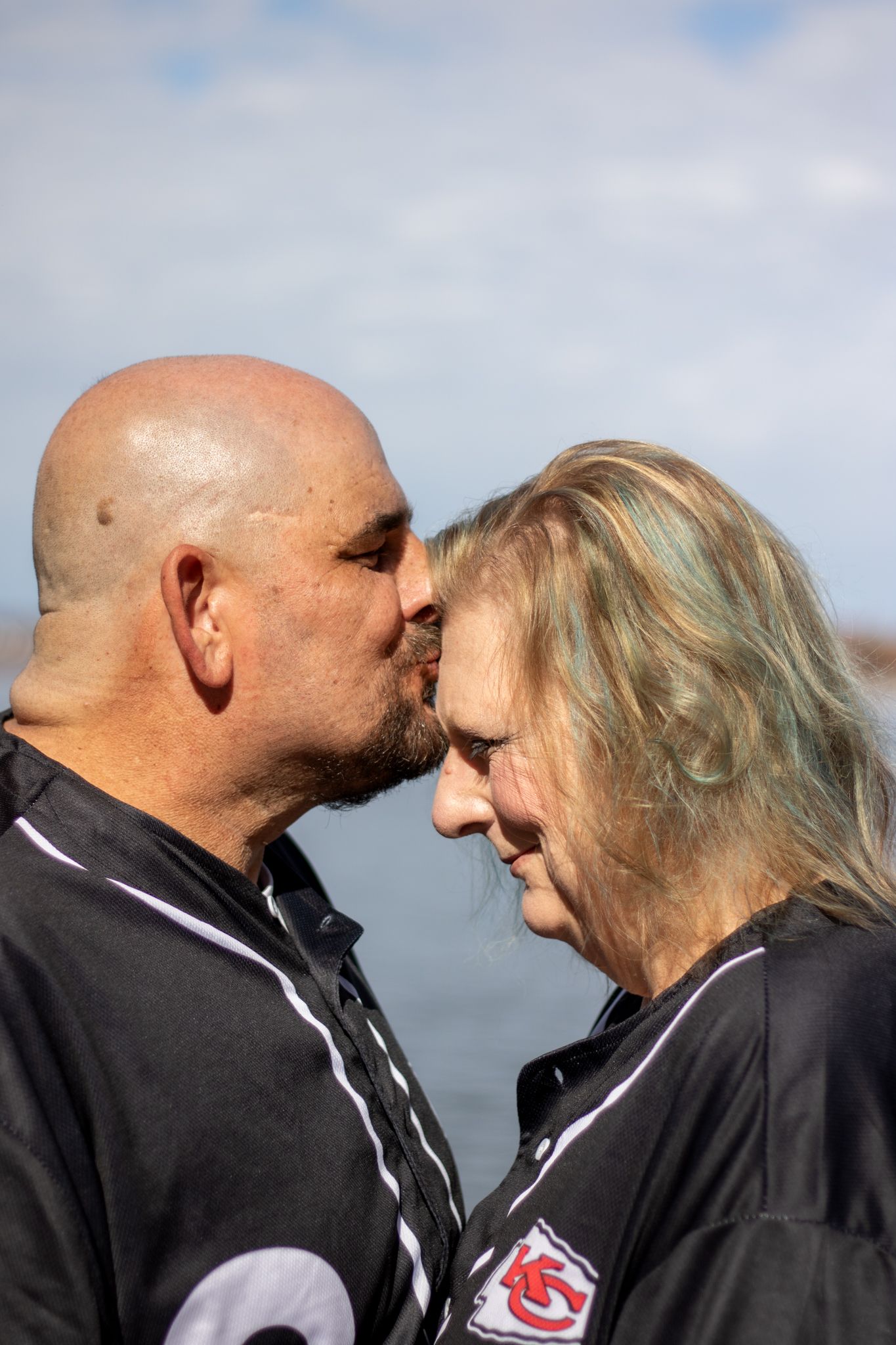 Husband kissing wifes forehead at lake.