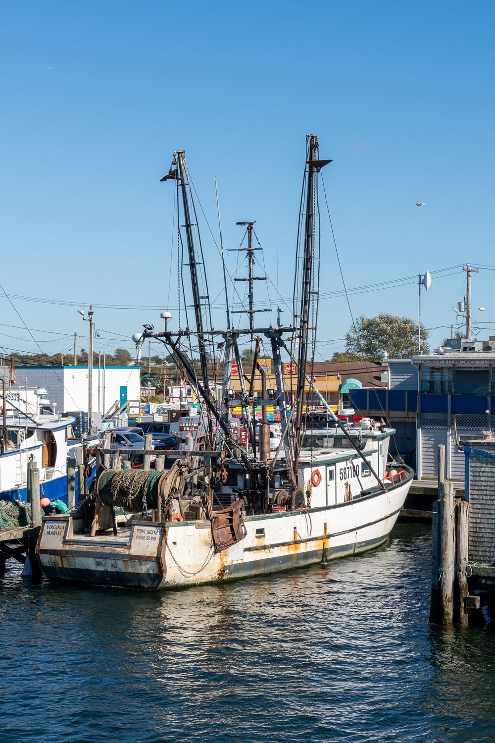 A commercial fishing boat with tall rigging docked at a marina with blue water.