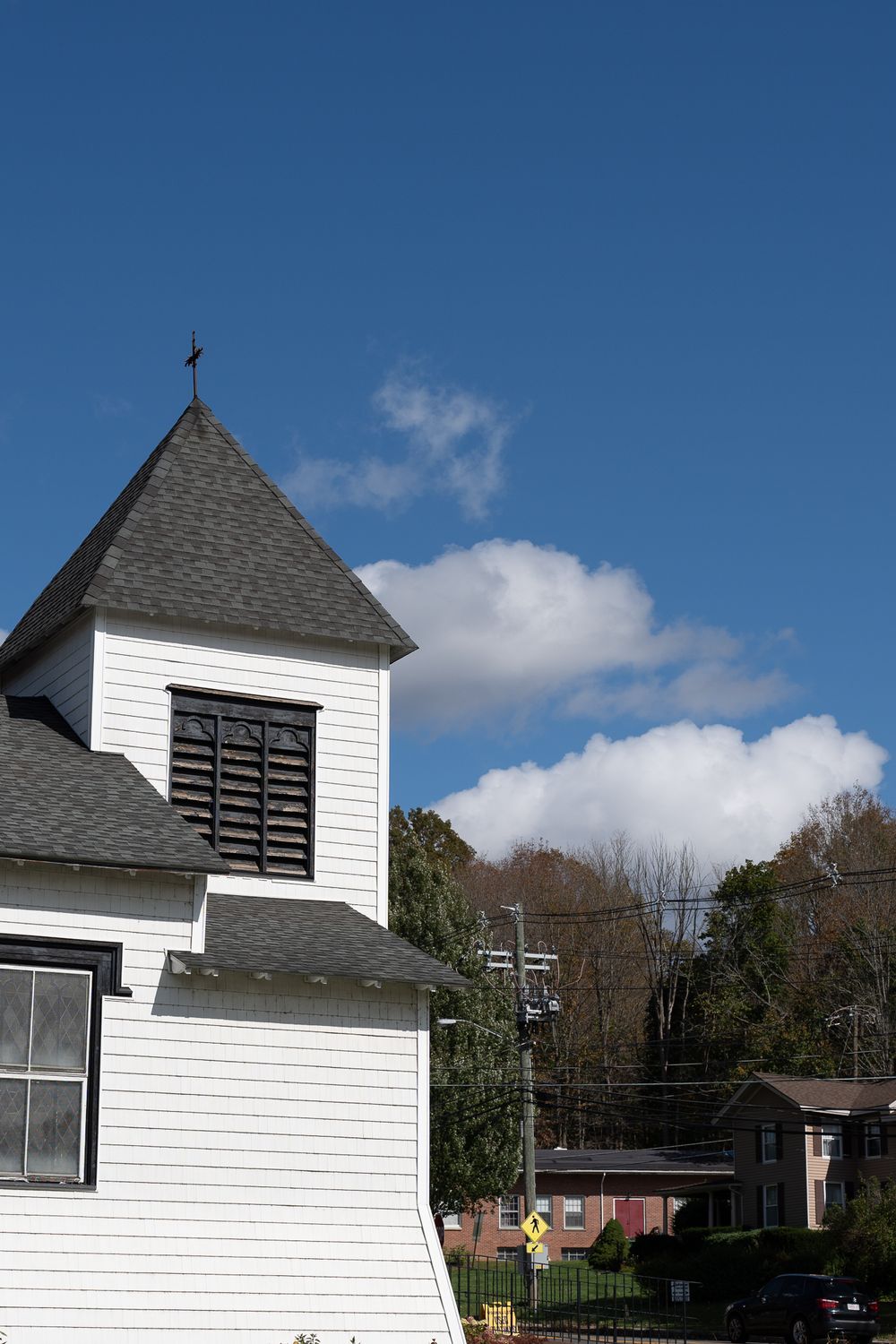 White church steeple with cross against blue sky and puffy white clouds.