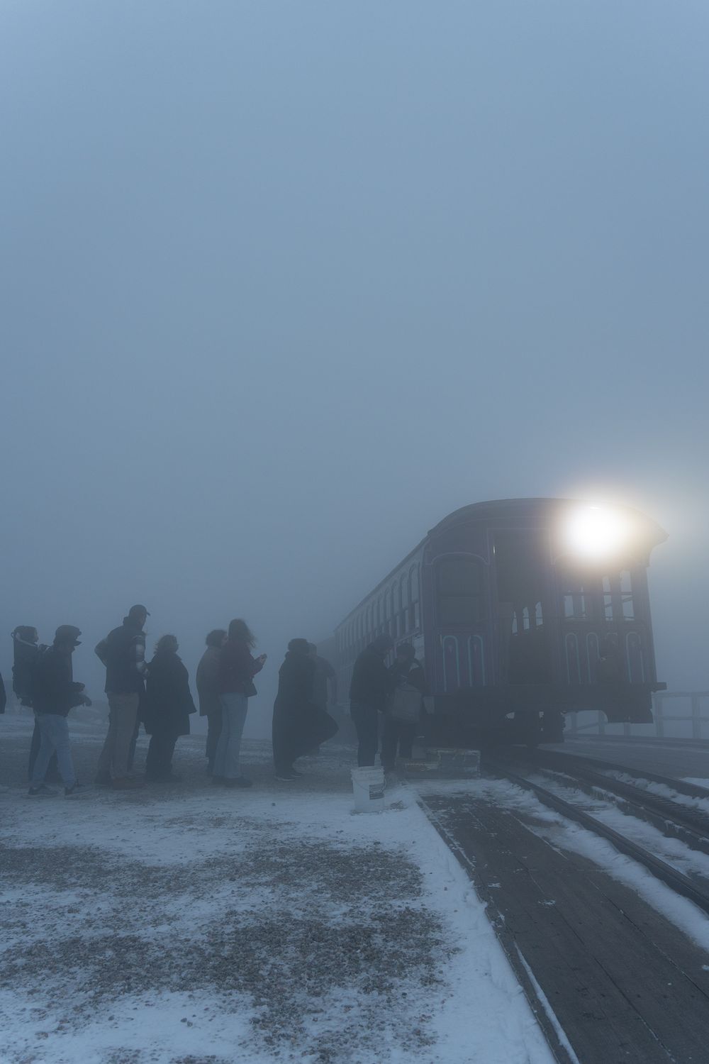 Silhouettes of people waiting by a train in heavy winter fog.