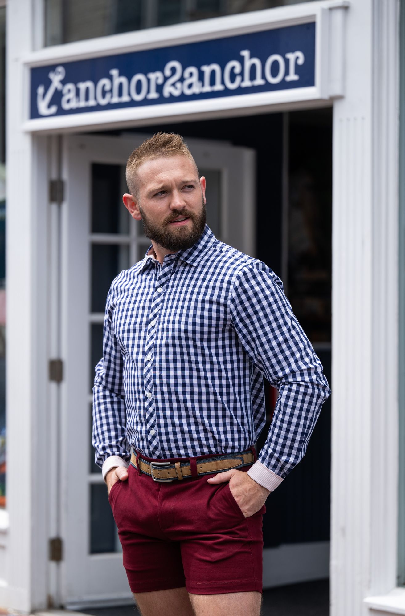 Person wearing gingham shirt and burgundy shorts posing outside Anchor & Arrow storefront.