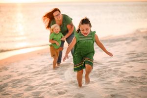 People in green outfits playing and running along a beach at sunset.