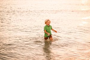 Child wading through shallow ocean water at sunset.