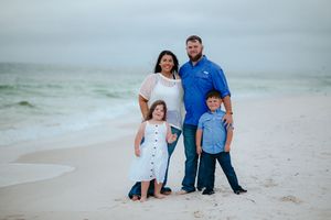 Family poses for casual beach portraits near ocean waves.