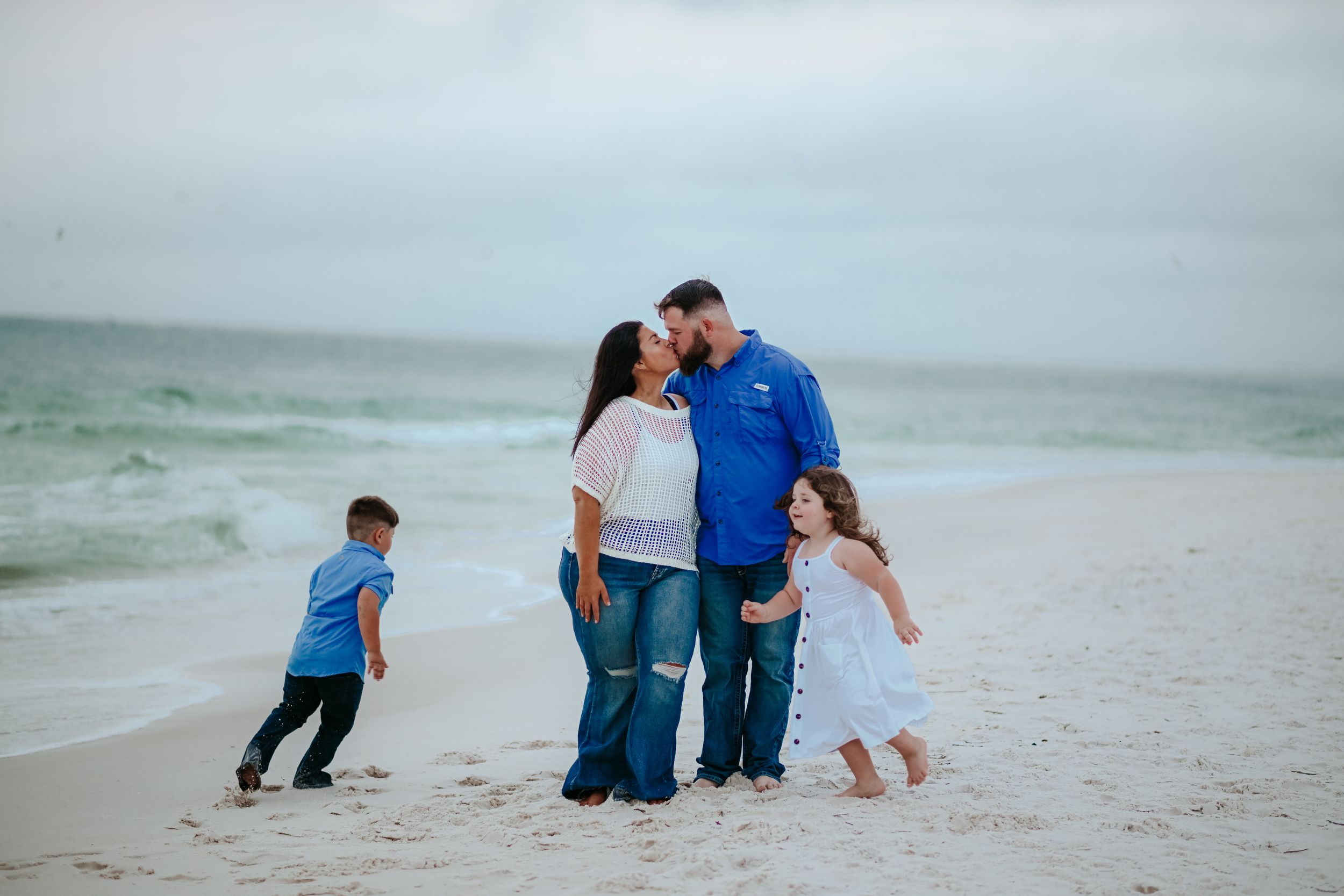 Family plays together on sandy beach during overcast day.