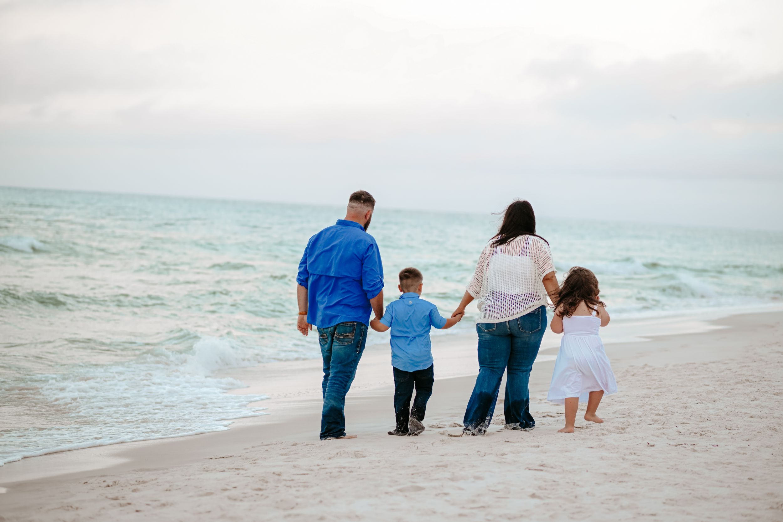 A family walks together along the shoreline during sunset at the beach.