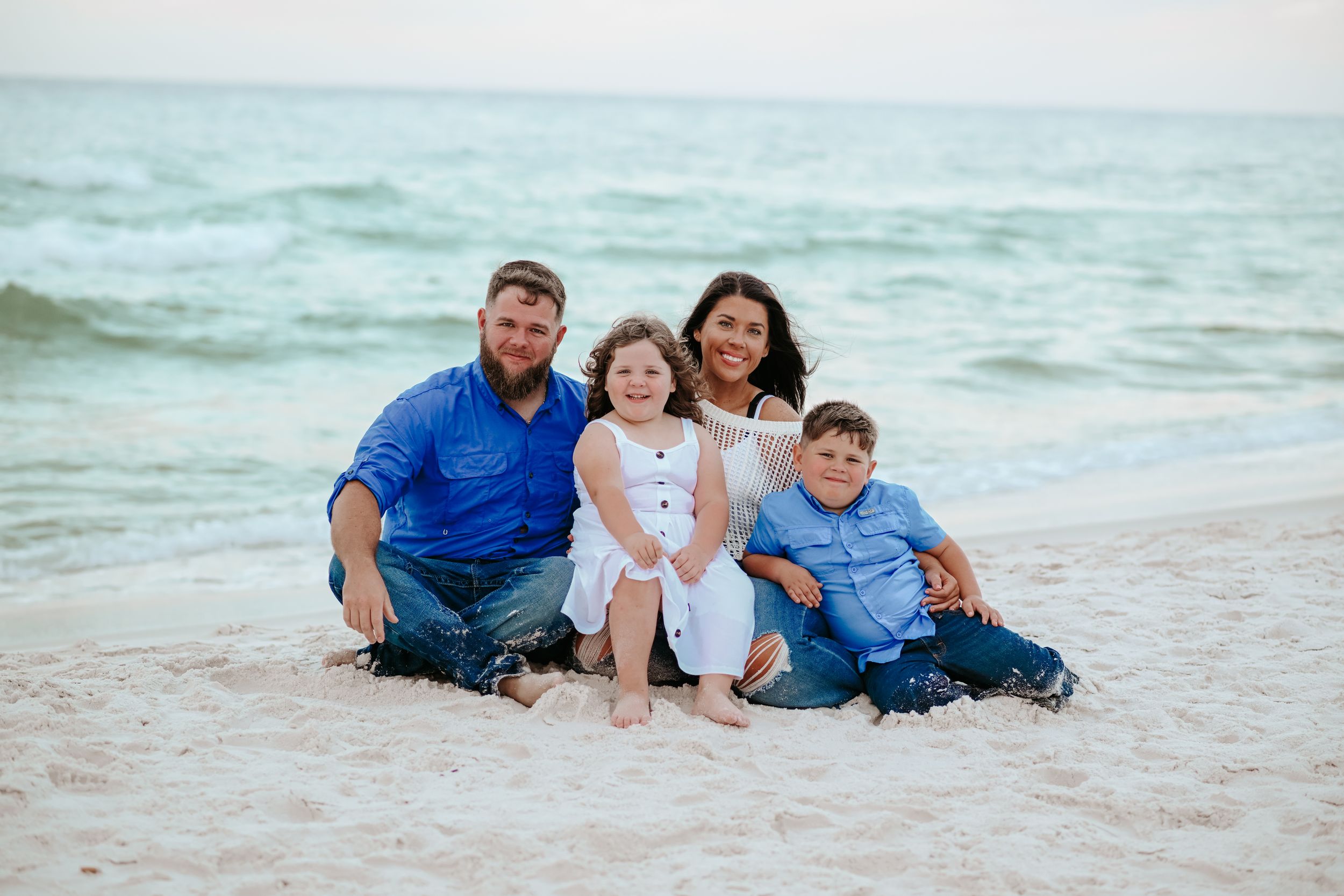 A family relaxes together on the sand during a beach photoshoot.