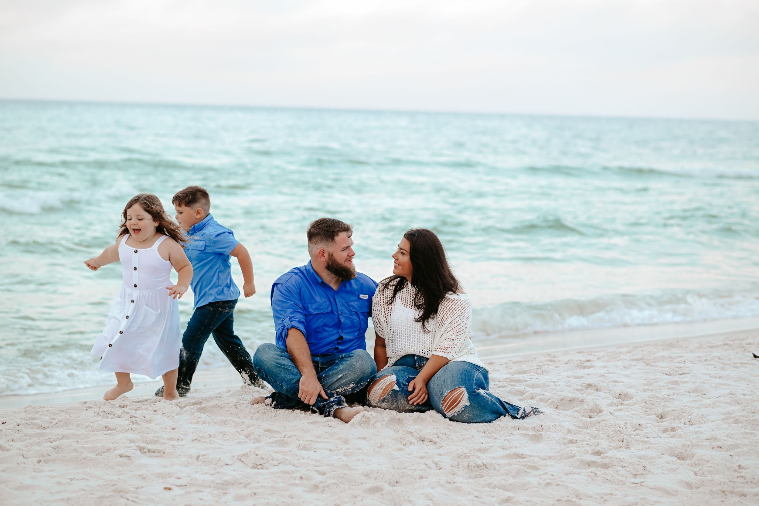 A family plays and laughs together while lying on the beach sand.