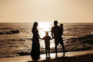 Silhouetted family figures walking together on beach at sunset.