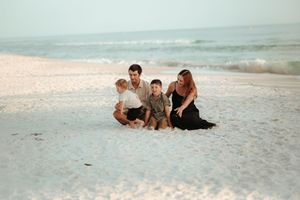 Family relaxing together on white sandy beach during sunset.