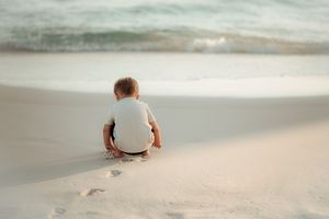 Child playing in white sand during beach sunset photoshoot.