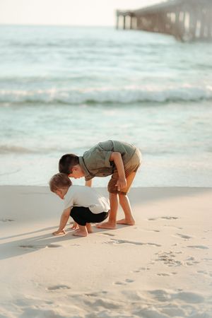 Two people search for seashells on a white sandy beach at sunset.