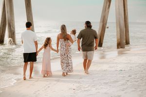 Beachgoers walk along the sand beneath wooden pier posts at sunset.
