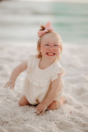 A child in a white dress plays in the soft white sand at the beach.