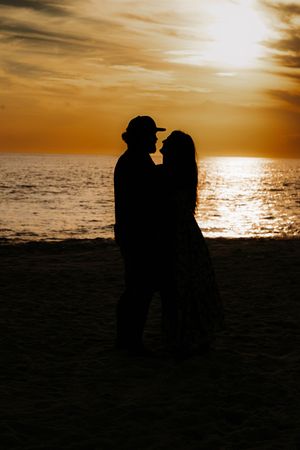 Silhouetted figures stand against a dramatic golden sunset over the ocean.
