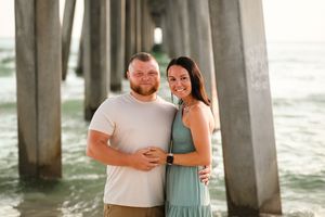 Couple shares intimate moment beneath beach pier at sunset.