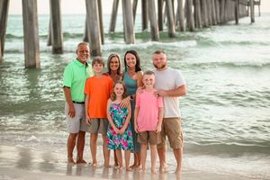 Family group photo under wooden pier with ocean waves in background.