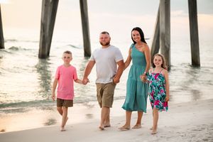 Family members stroll along beach near wooden pier during sunset.