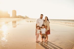 Family of four walking together on a sandy beach at sunset.
