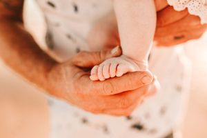 A tiny baby's hand gently rests in an adult's palm in a tender moment.