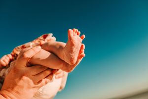 Small baby feet being held up against a bright turquoise sky background.